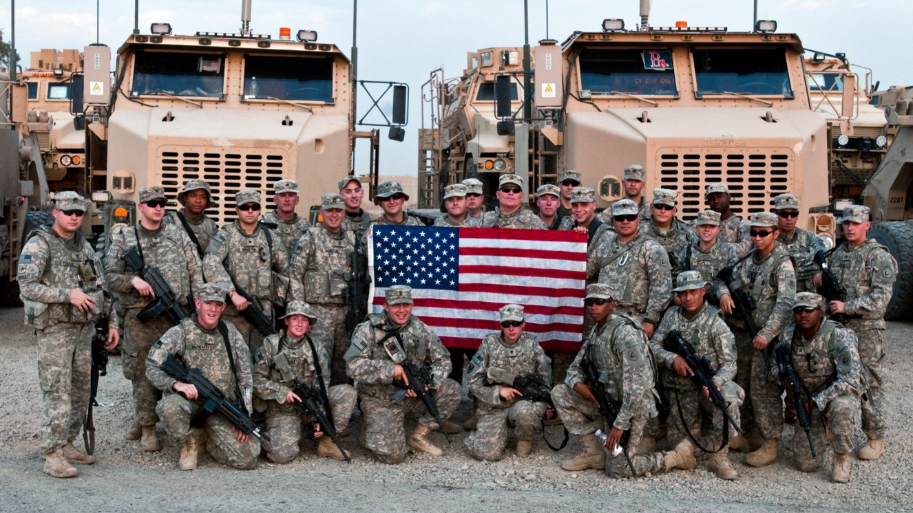 Soldiers with 2nd platoon, 1166th Combat Heavy Equipment Transport Company, 164th Transportation Battalion, pose with an American flag on Contingency Operating Base Speicher, Iraq. Units like this continue to operate due to the 2022 Iraq War authorization.