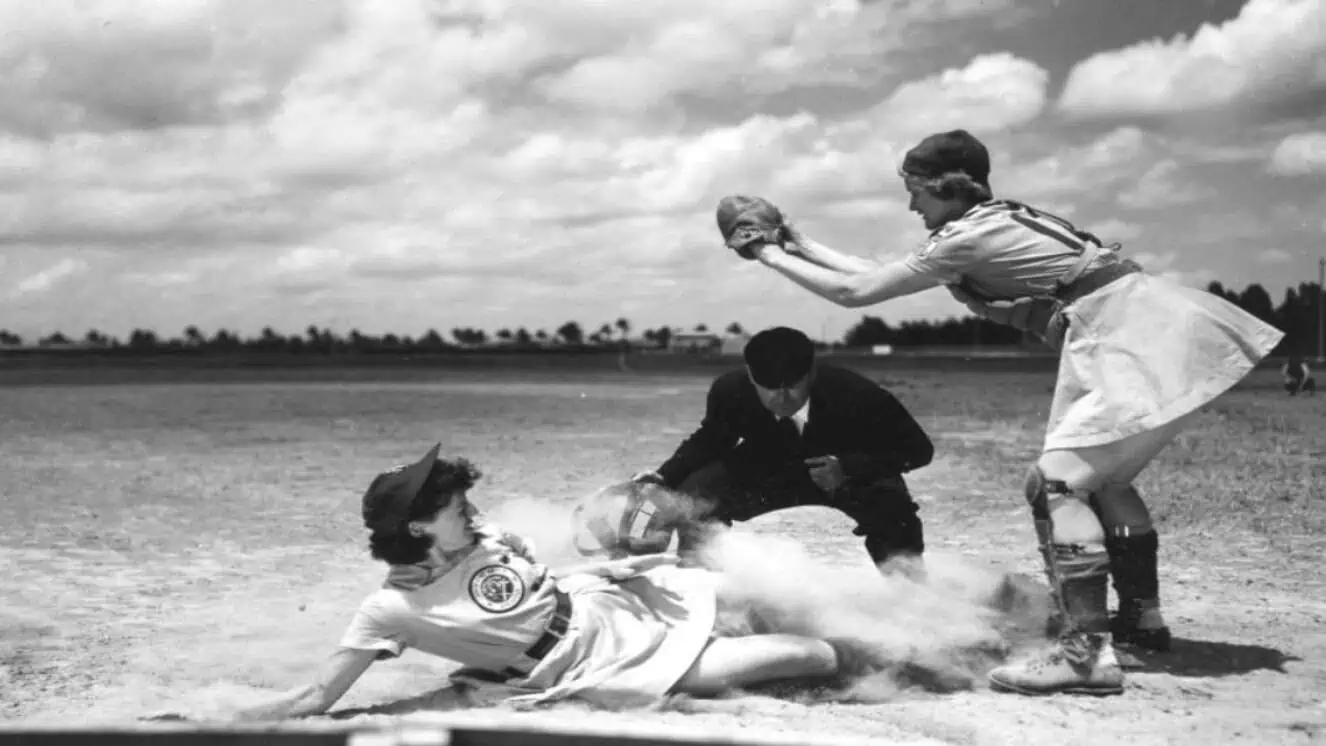 All-American Girls Professional Baseball League Player Marg Callaghan Sliding into Home Plate as Umpire Norris Ward Watches. The history of softball begins with the AAGPBL.