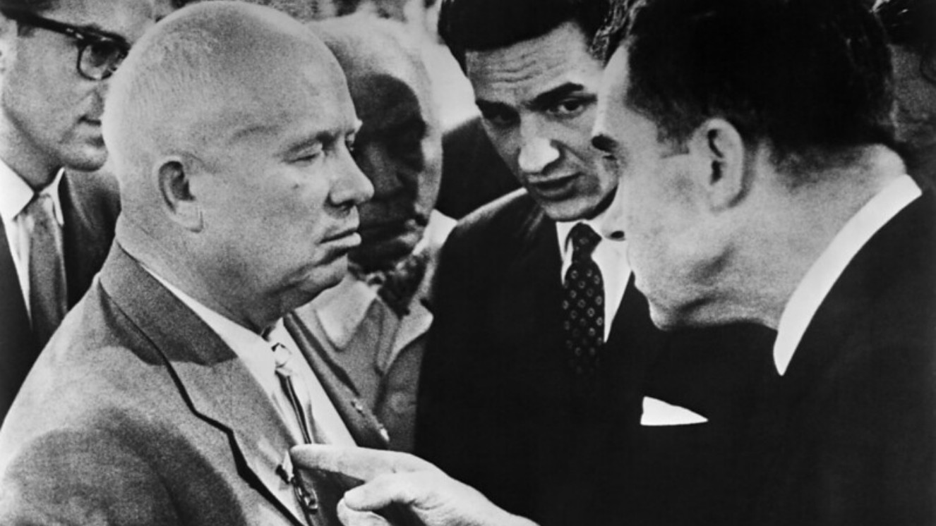 Vice President Richard Nixon touches the chest of Soviet Premier Nikita Khrushchev during a conversation at the Kitchen Debate. Translators and officials surround the men.
