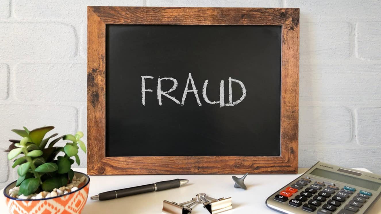 Written on a chalkboard on top of a desk is the word fraud. Veteran fraud is dangerous and on the rise.