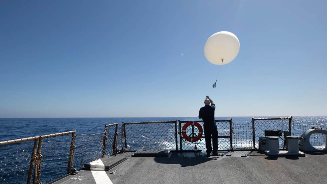 A Chinese balloon flying in the sky off a boat.