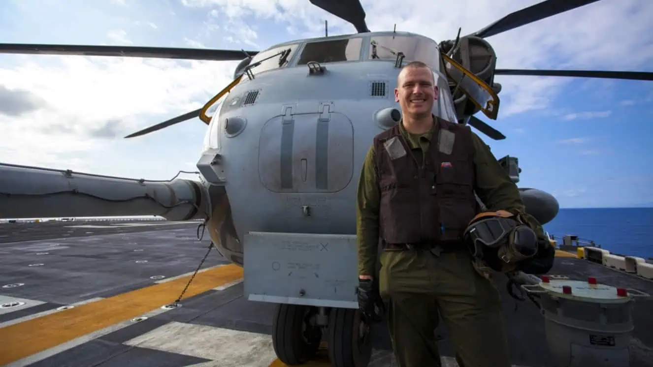 Lance Cpl. Landon Smith stands in front of a CH-53E Super Stallion on the flight deck of amphibious assault ship USS America during RIMPAC.